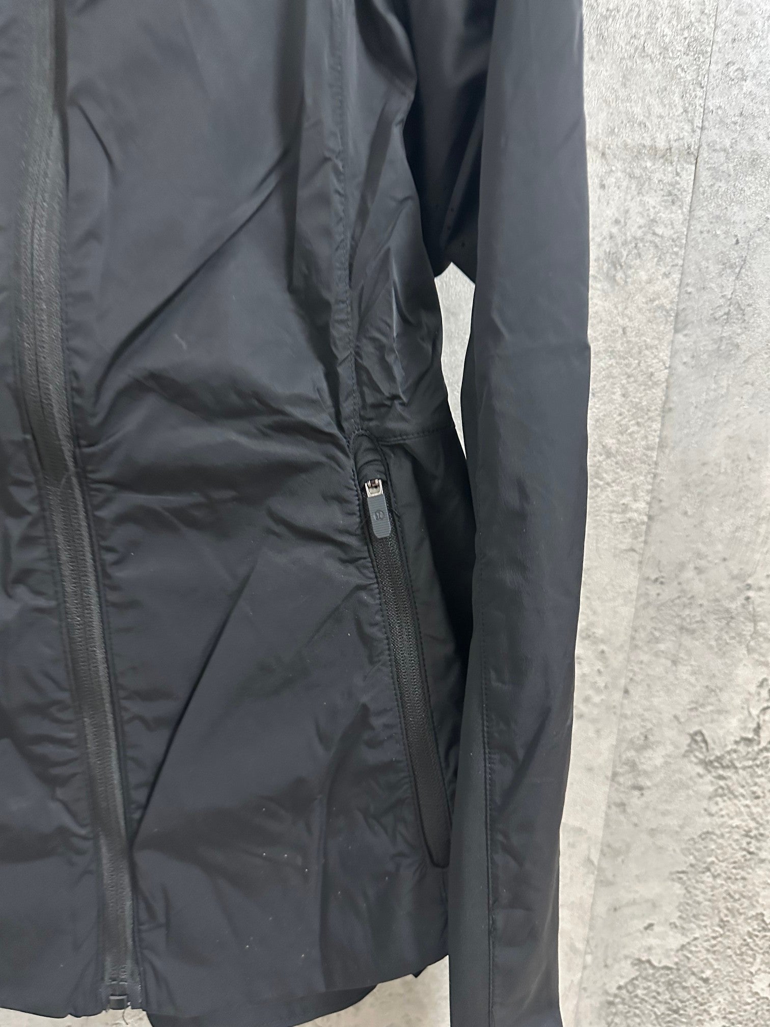 Hooded rain jacket side close-up with zipper pocket and seam details, dark color