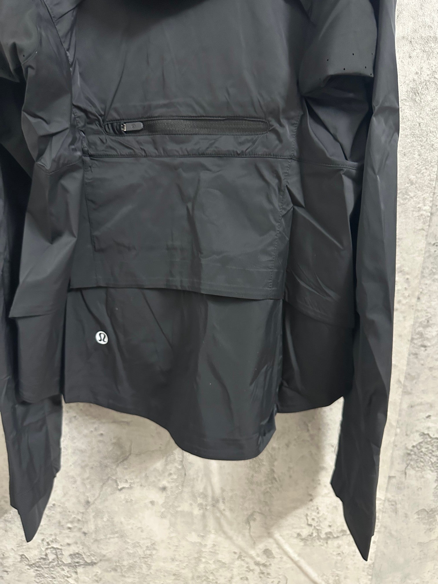 Hooded rain jacket back panel close-up with patch pocket and zipper accents, dark color