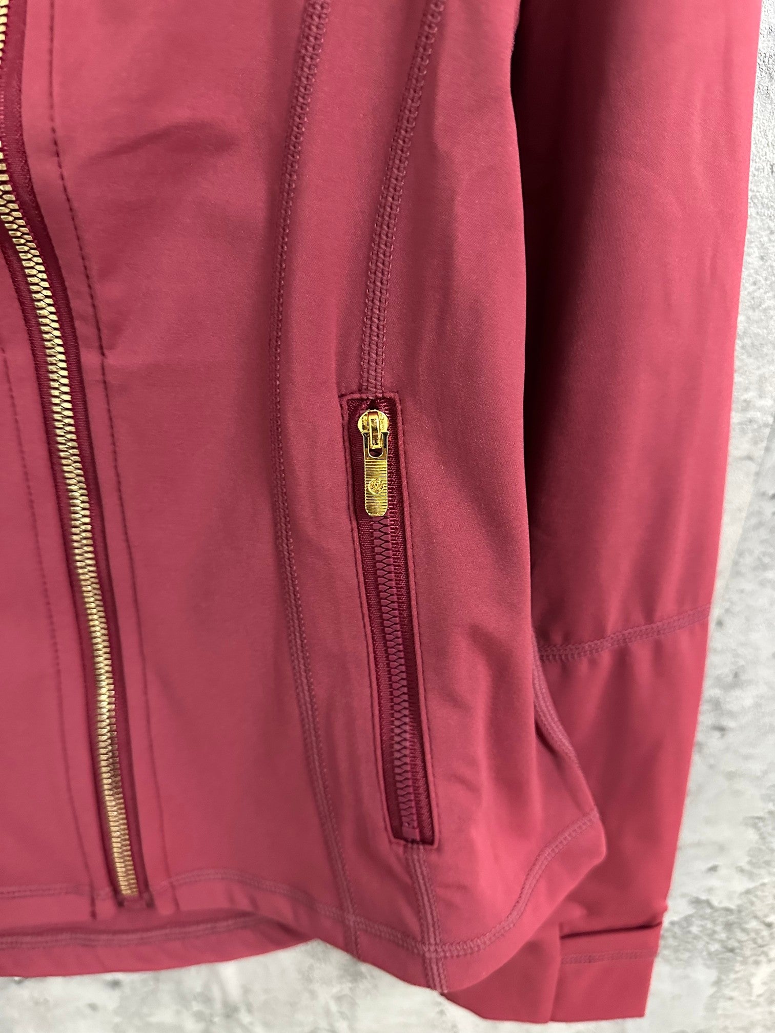 Burgundy jacket sleeve and side seam with gold zip pocket detail