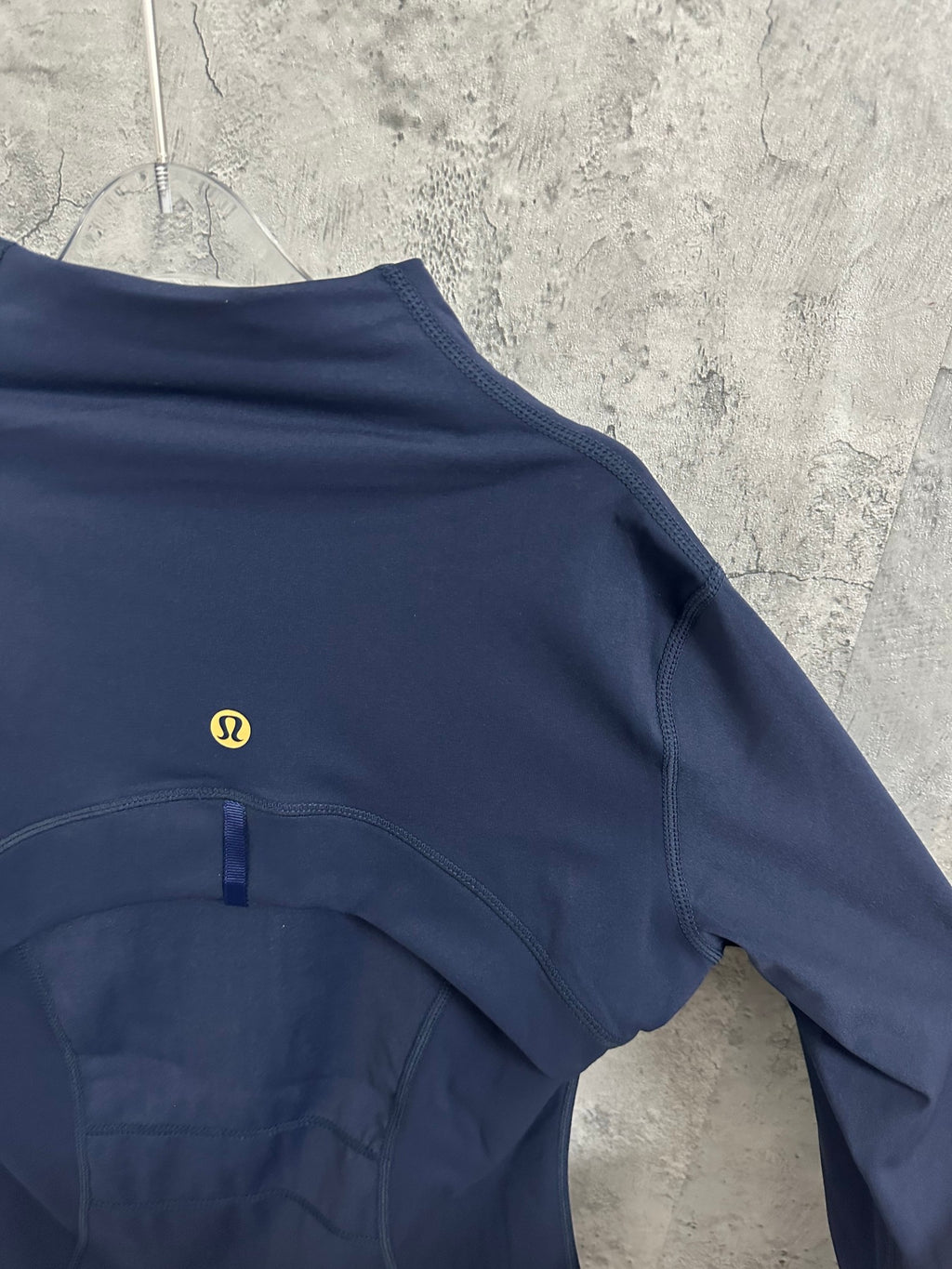 Navy jacket back yoke with small gold logo and curved seam stitching