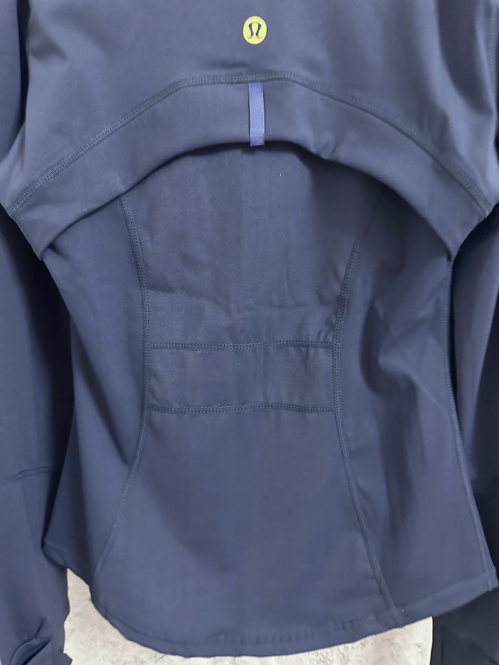 Navy jacket back with curved yoke seam and small gold logo at upper back