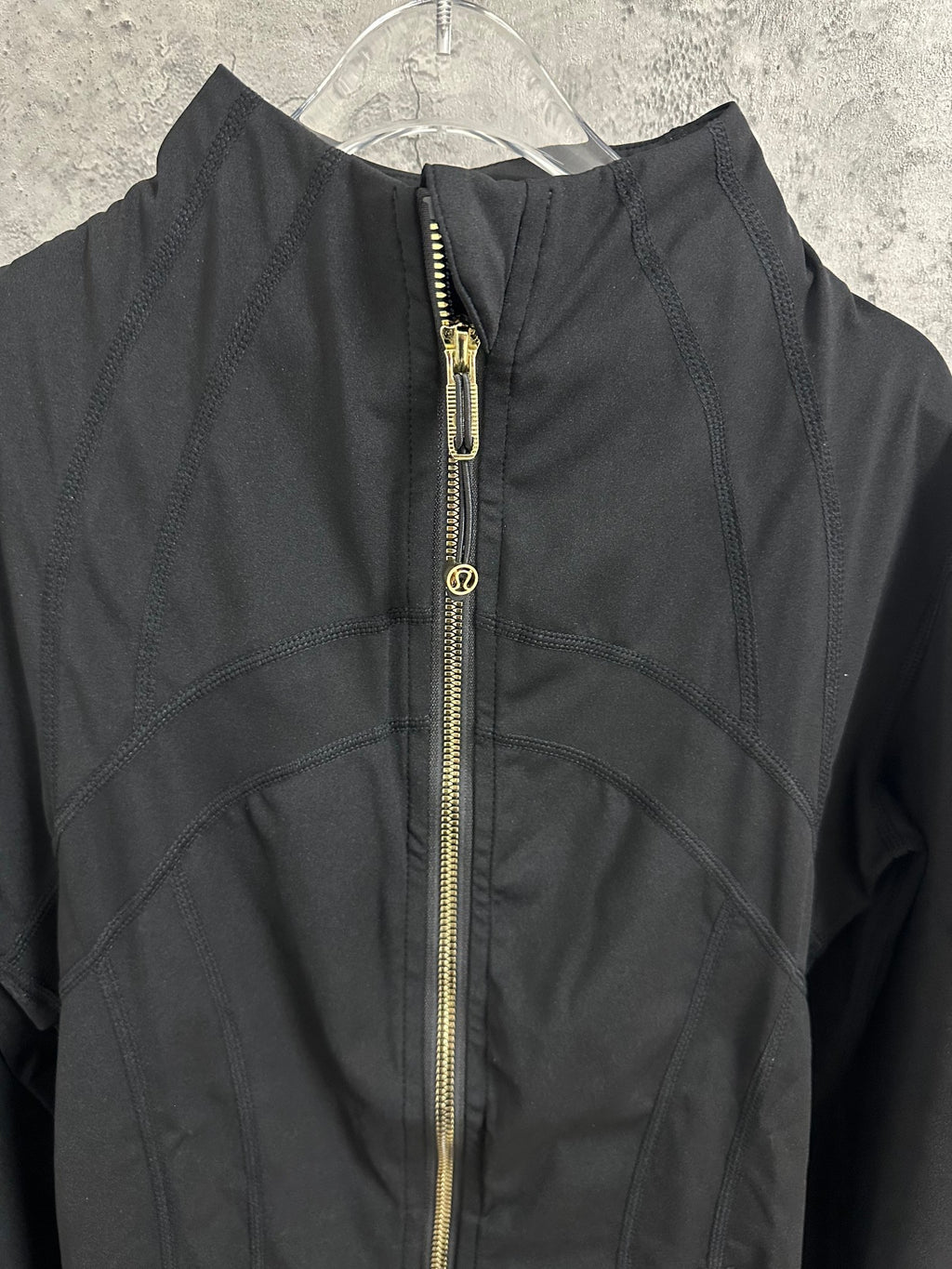 Black jacket close-up with center gold-tone zipper and logo pull