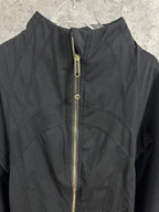 Black jacket close-up with center gold-tone zipper and logo pull