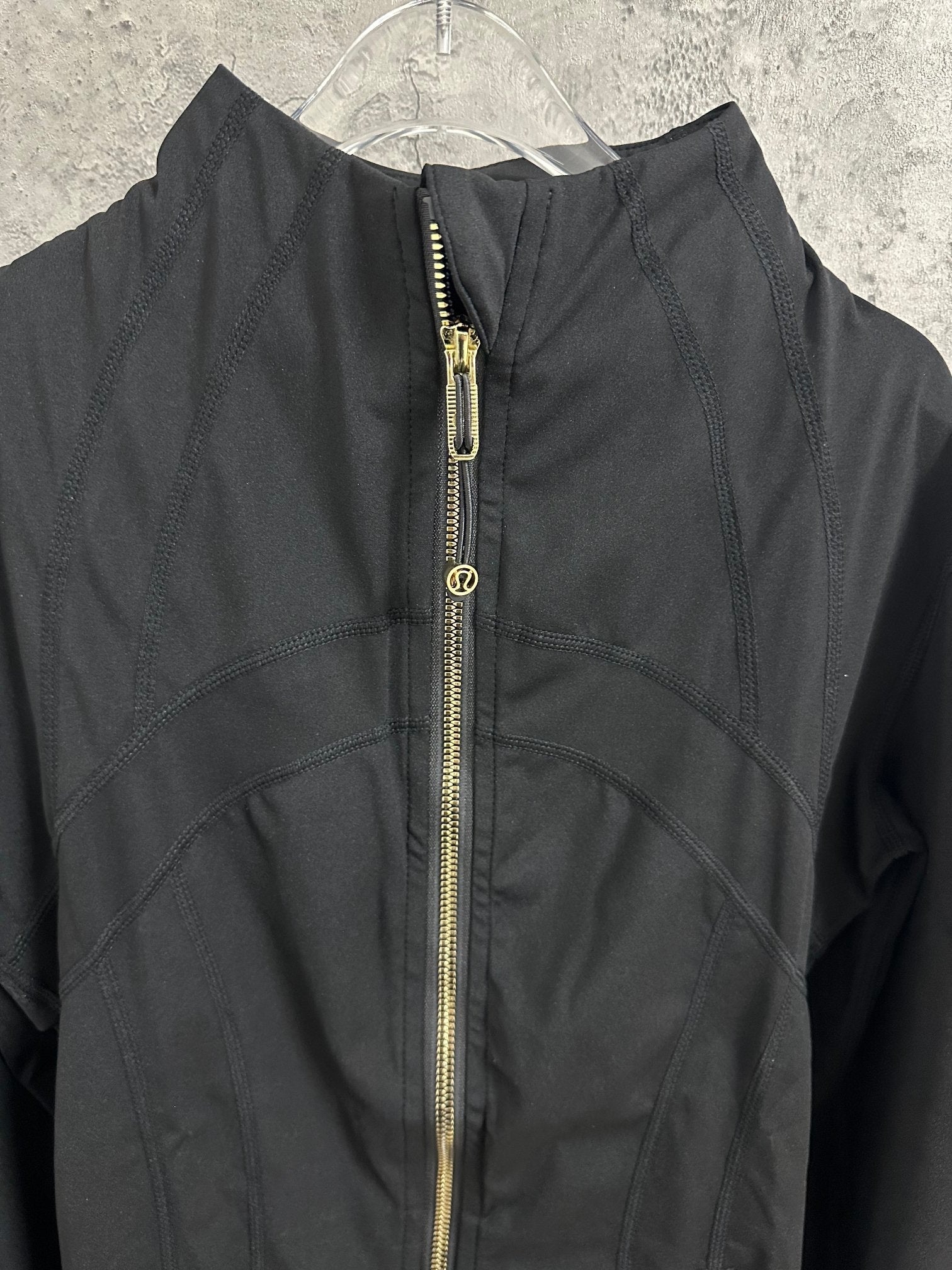 Black jacket close-up with center gold-tone zipper and logo pull