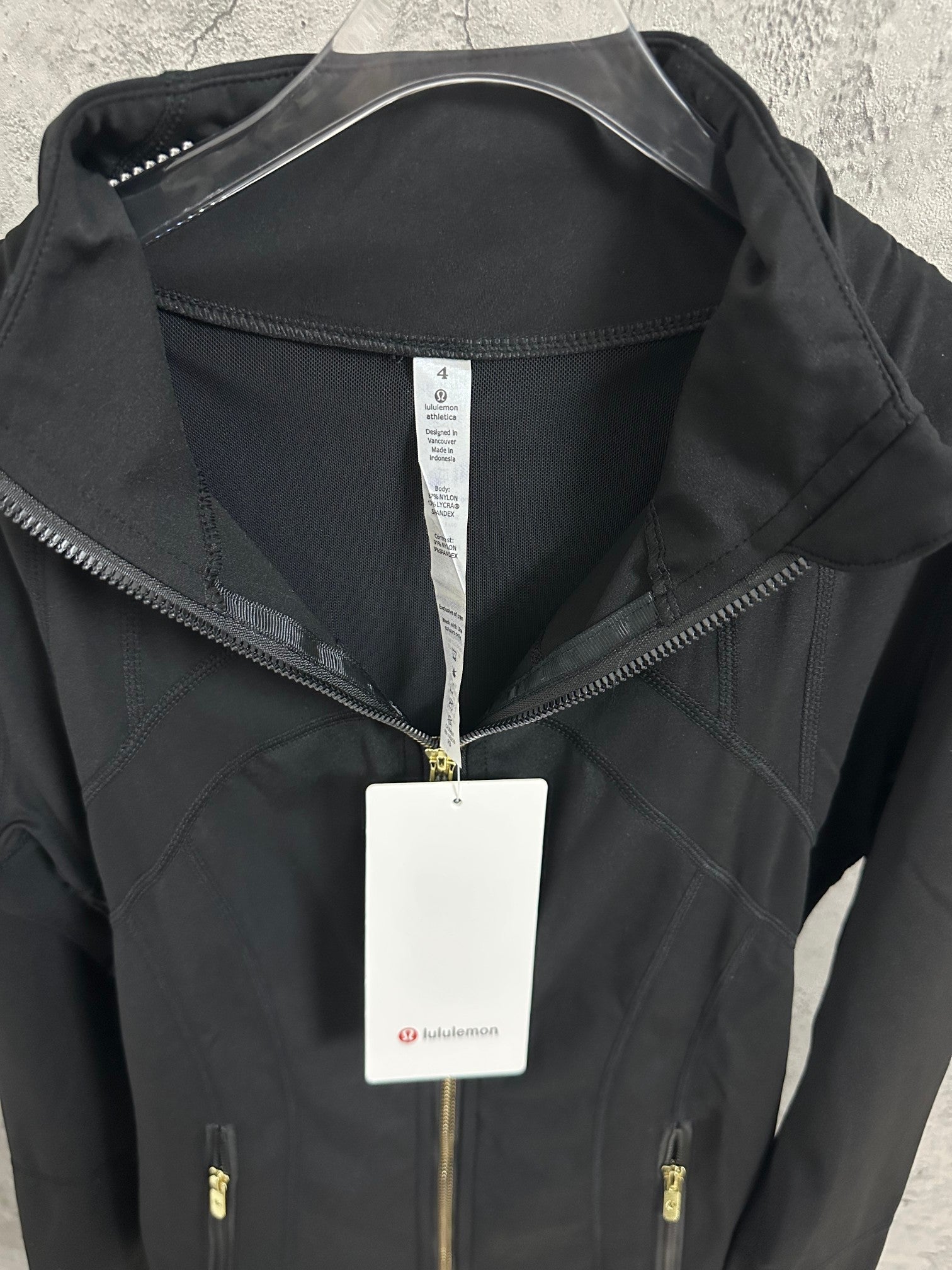Black jacket with high collar, gold-tone zipper, and white size label