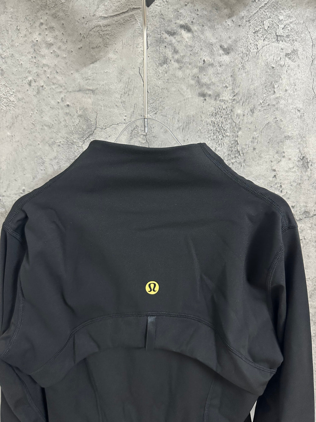 Black jacket back view with small gold logo at center