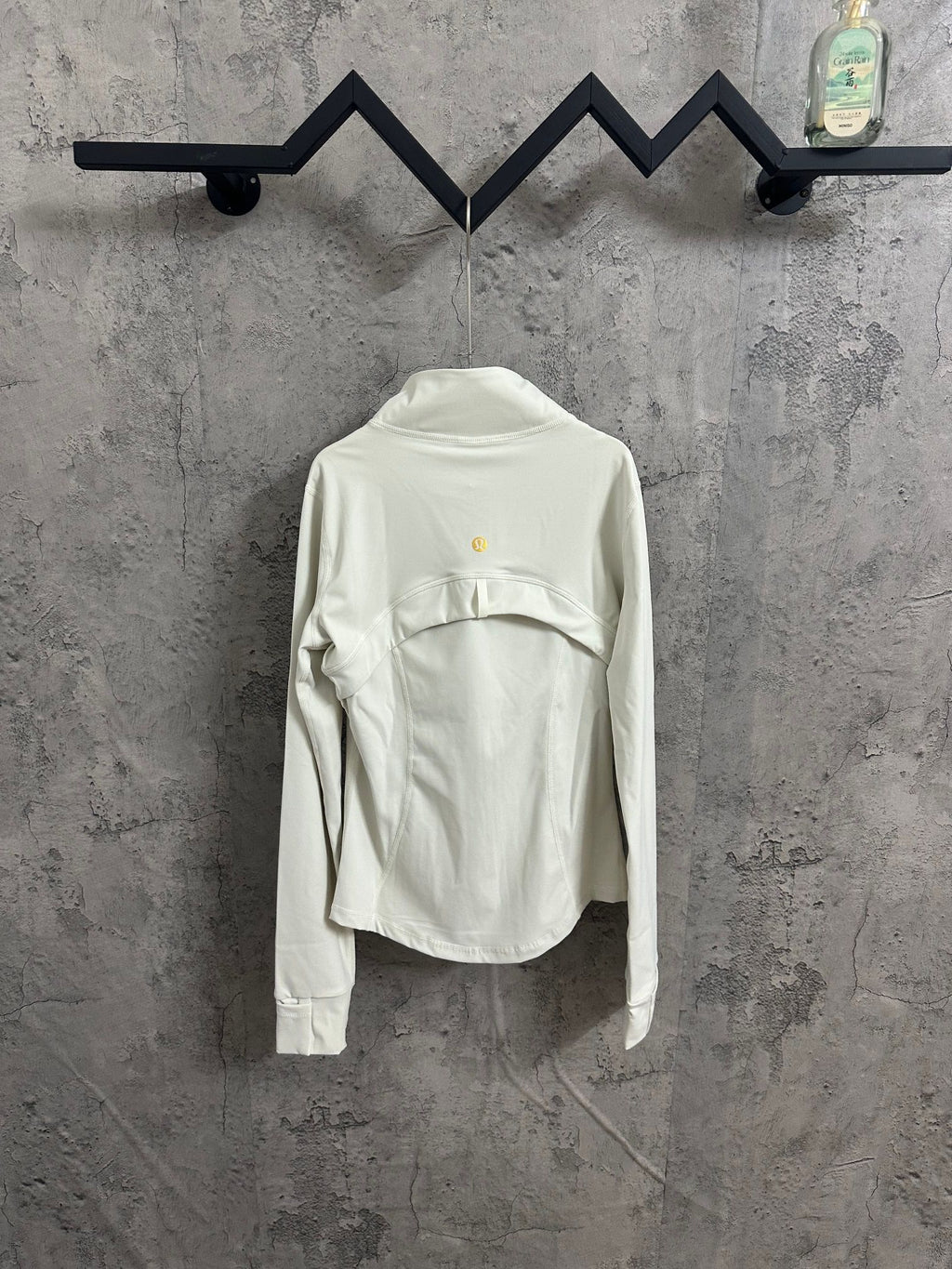 Light white zip-up jacket back view with stand collar and small gold logo at upper back.