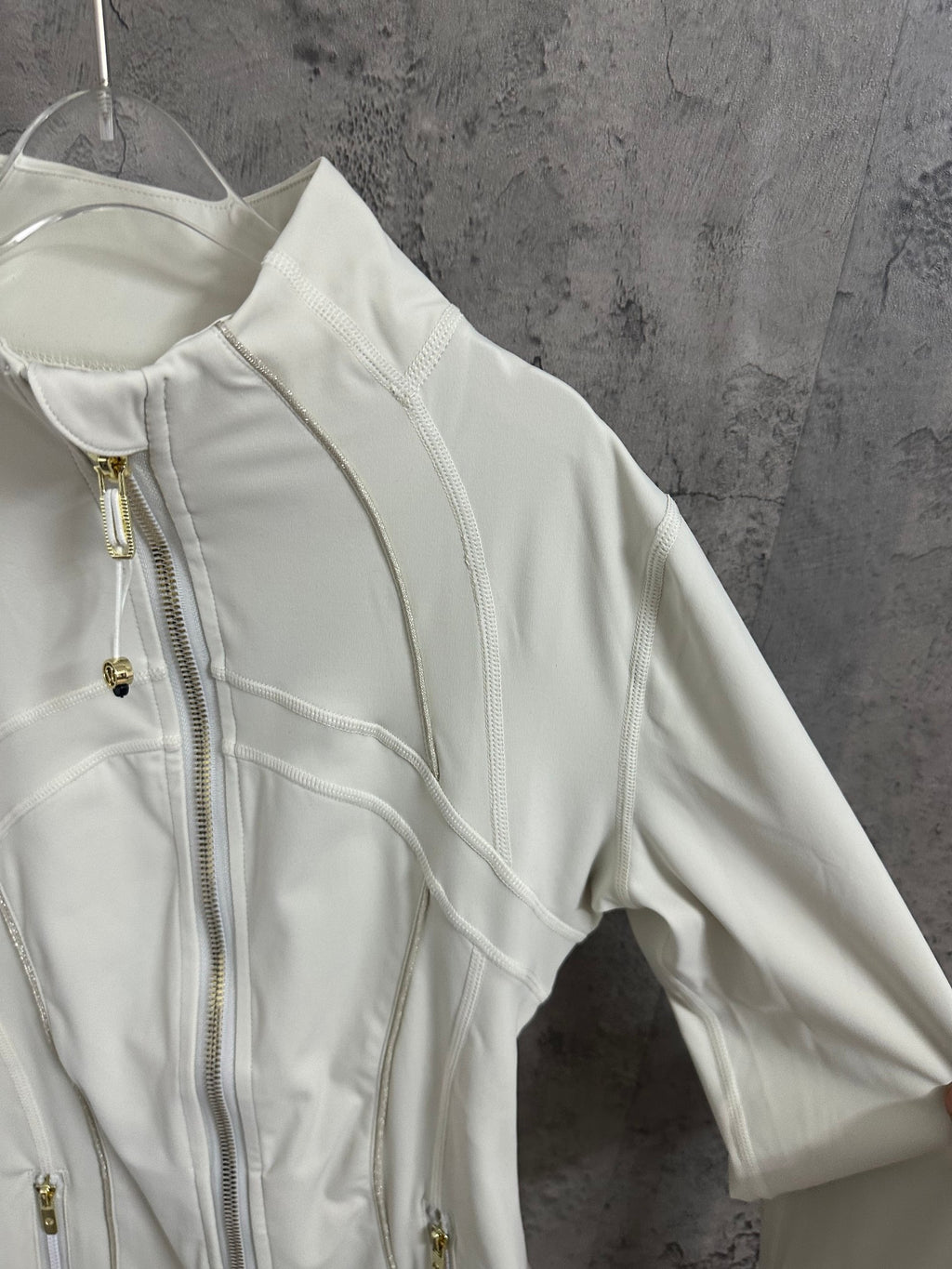 Light white zip-up jacket sleeve and shoulder detail with gold zipper hardware and curved seams.