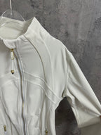 Light white zip-up jacket sleeve and shoulder detail with gold zipper hardware and curved seams.