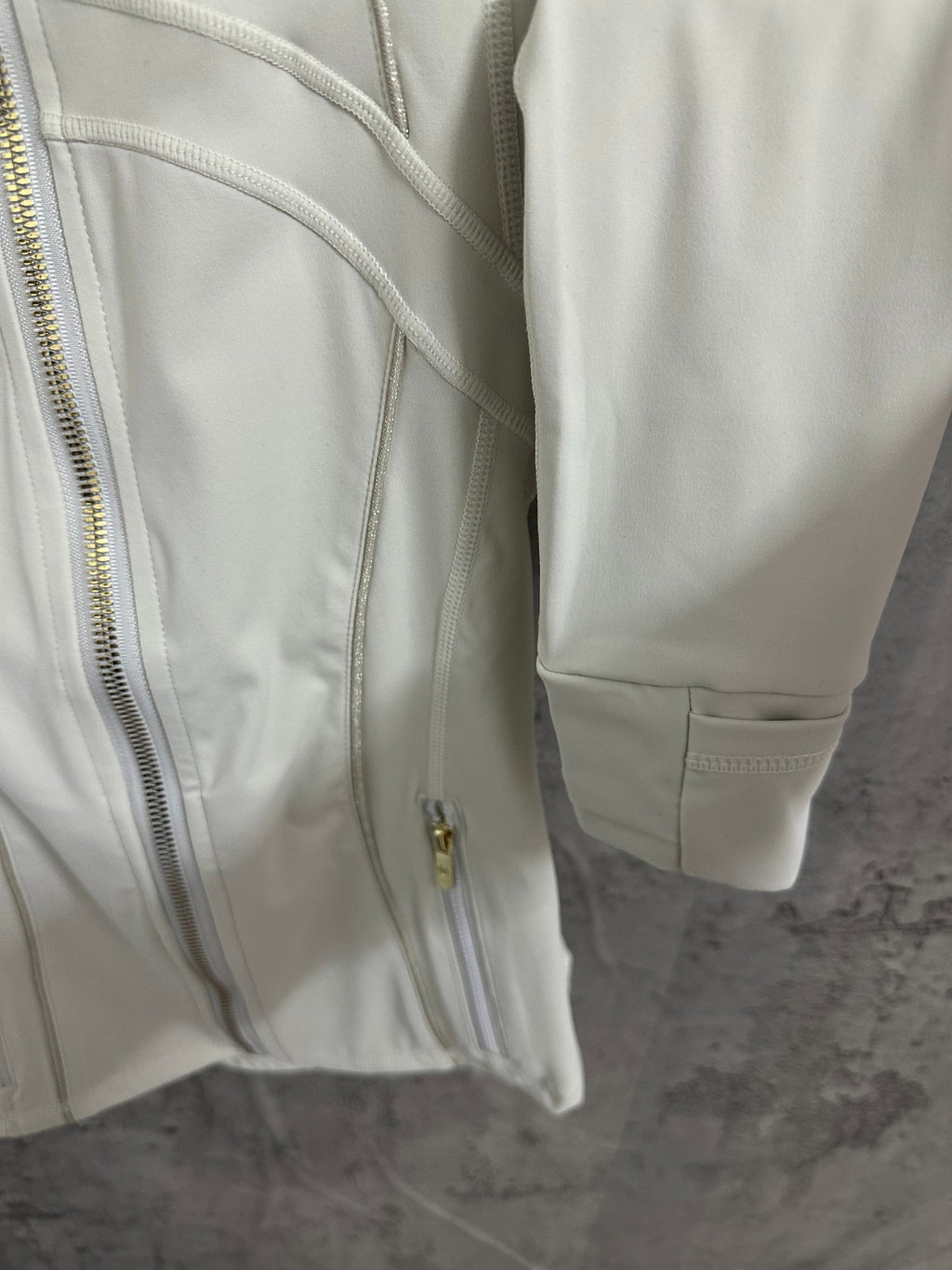 Light white zip-up jacket side detail with gold zipper and cuff, showing pocket opening.