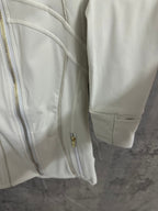 Light white zip-up jacket side detail with gold zipper and cuff, showing pocket opening.