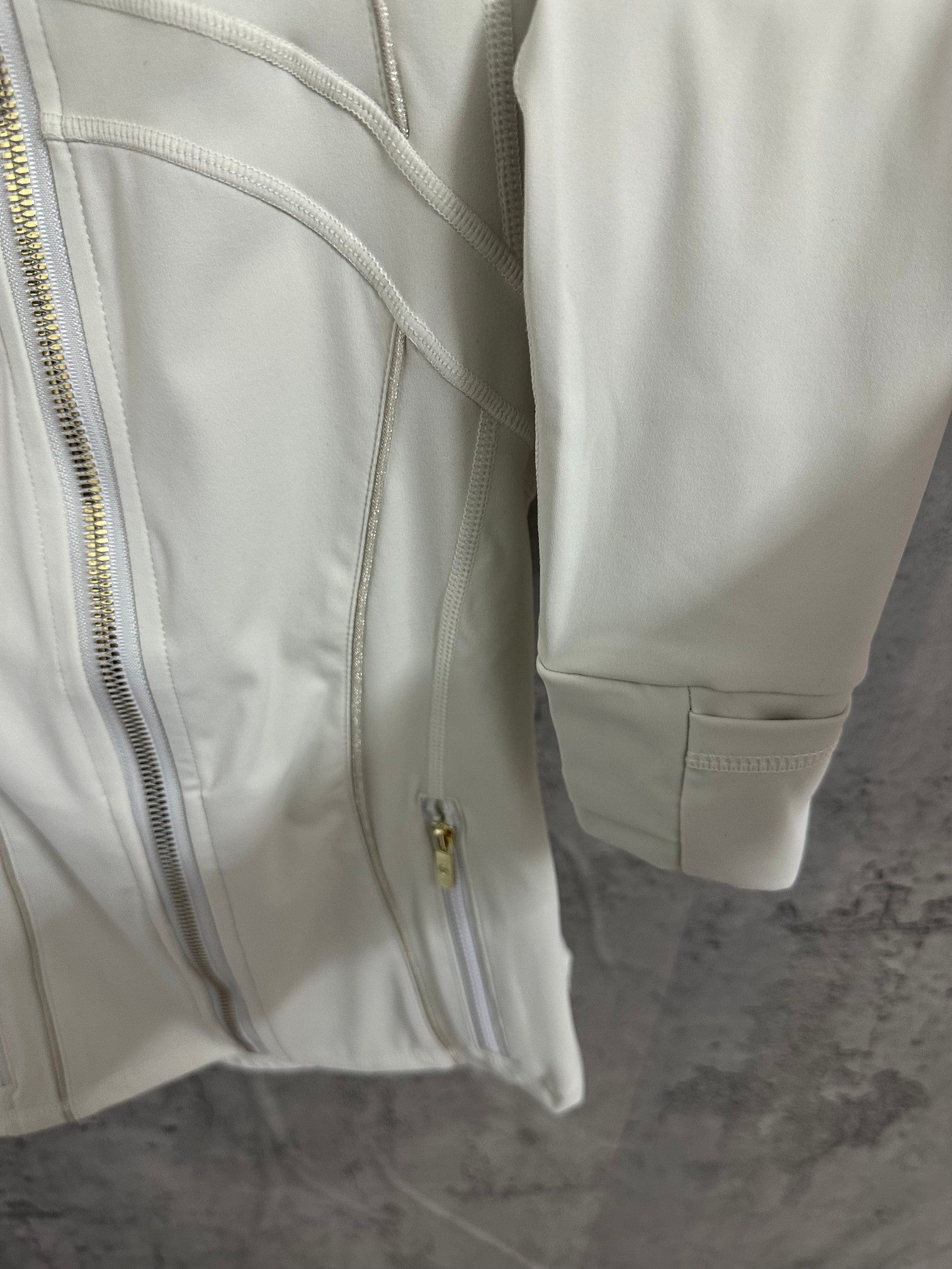 Light white zip-up jacket side detail with gold zipper and cuff, showing pocket opening.