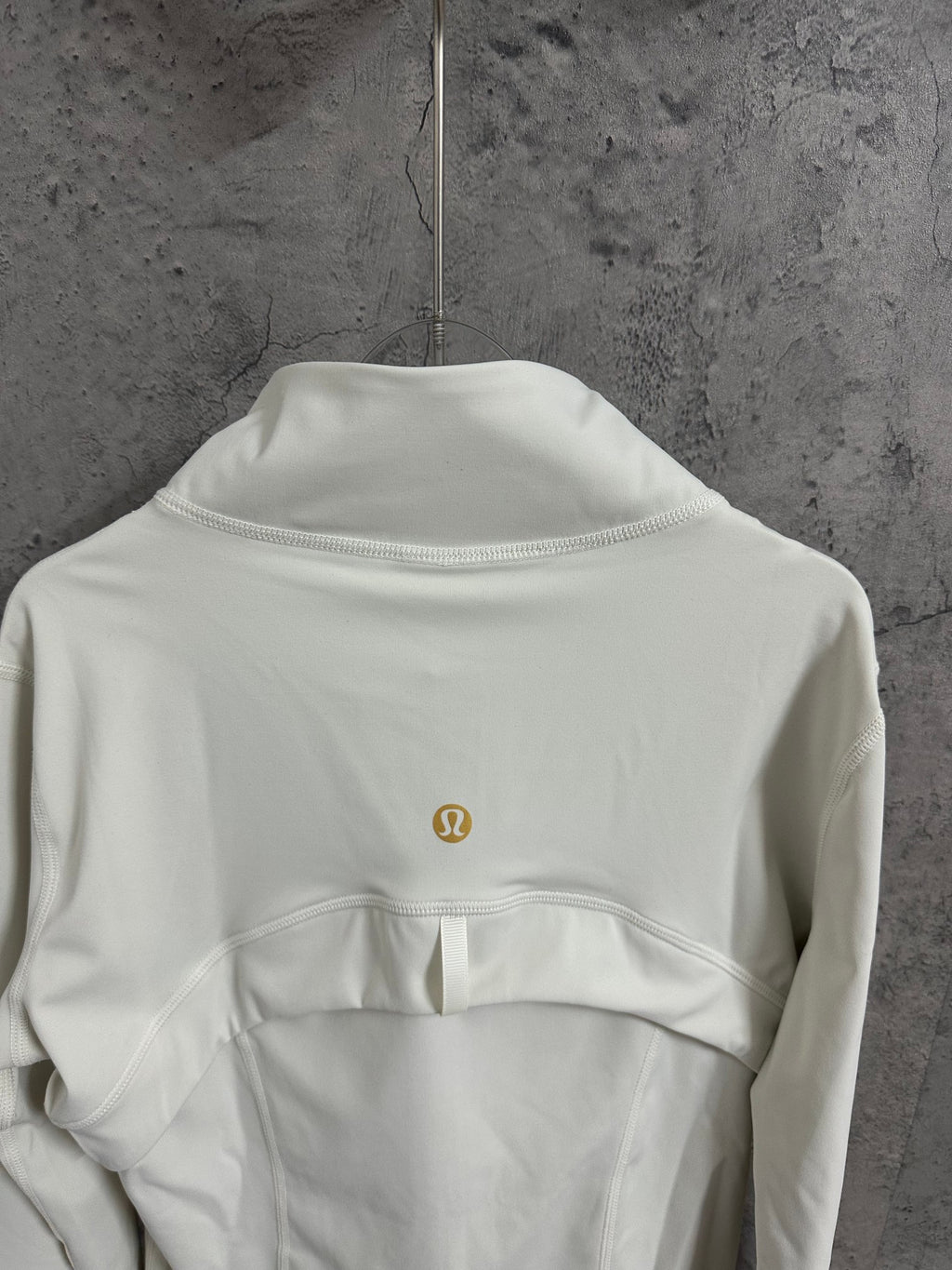 Light white zip-up jacket back neckline detail with stand collar and small gold logo.
