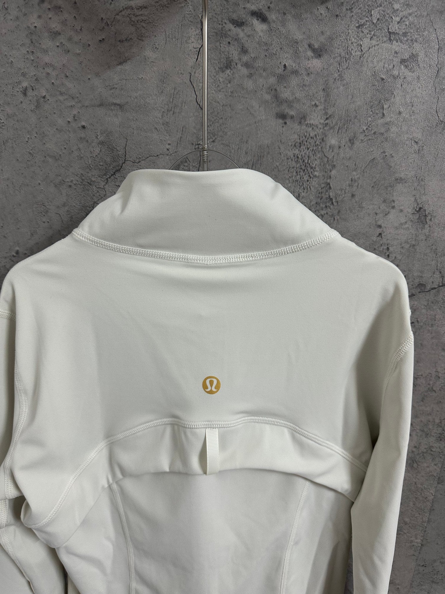Light white zip-up jacket back neckline detail with stand collar and small gold logo.