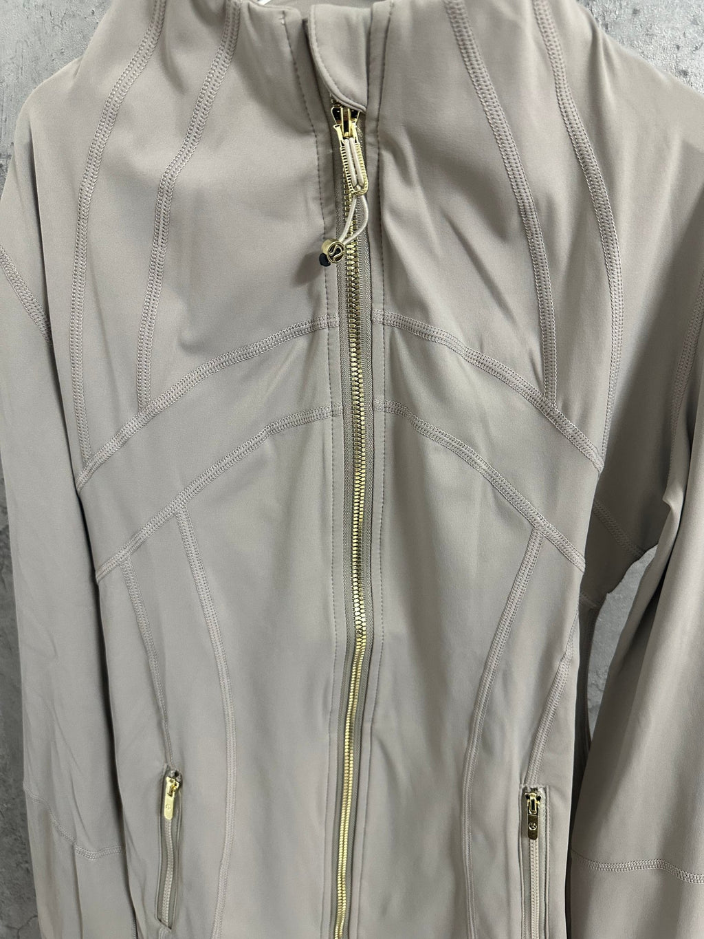 Beige jacket front with gold zipper and visible seam stitching, close-up
