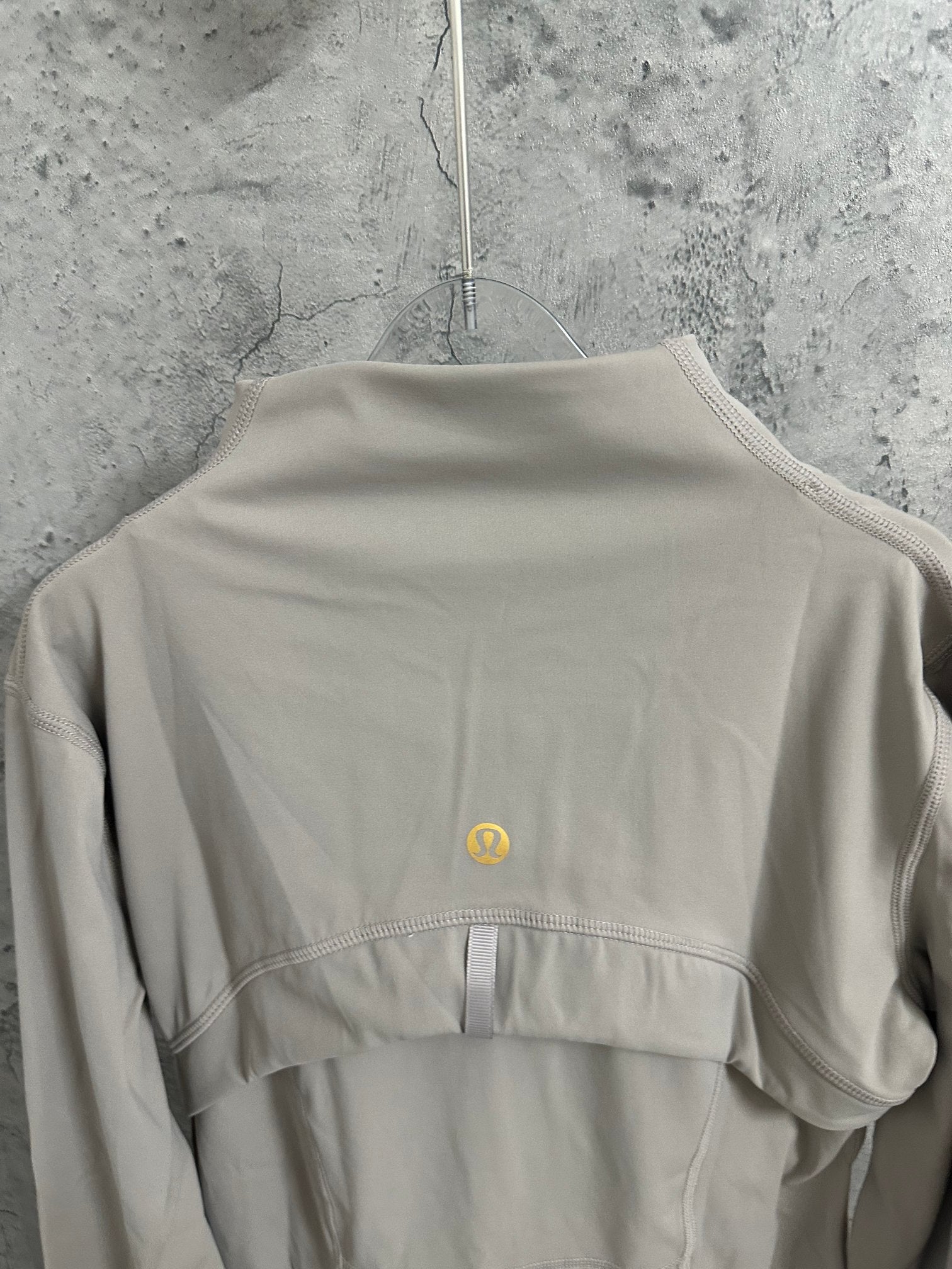 Light beige jacket back view with small yellow logo at upper back
