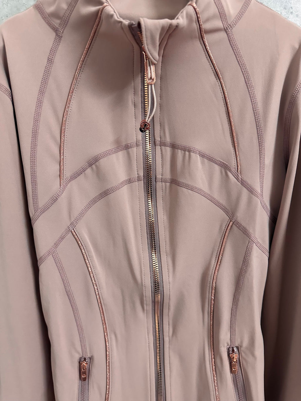 Dusty pink jacket front with central zipper and curved contrast stitch lines