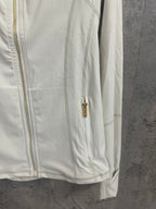 White jacket side view with gold zipper pull and stand collar; long sleeves