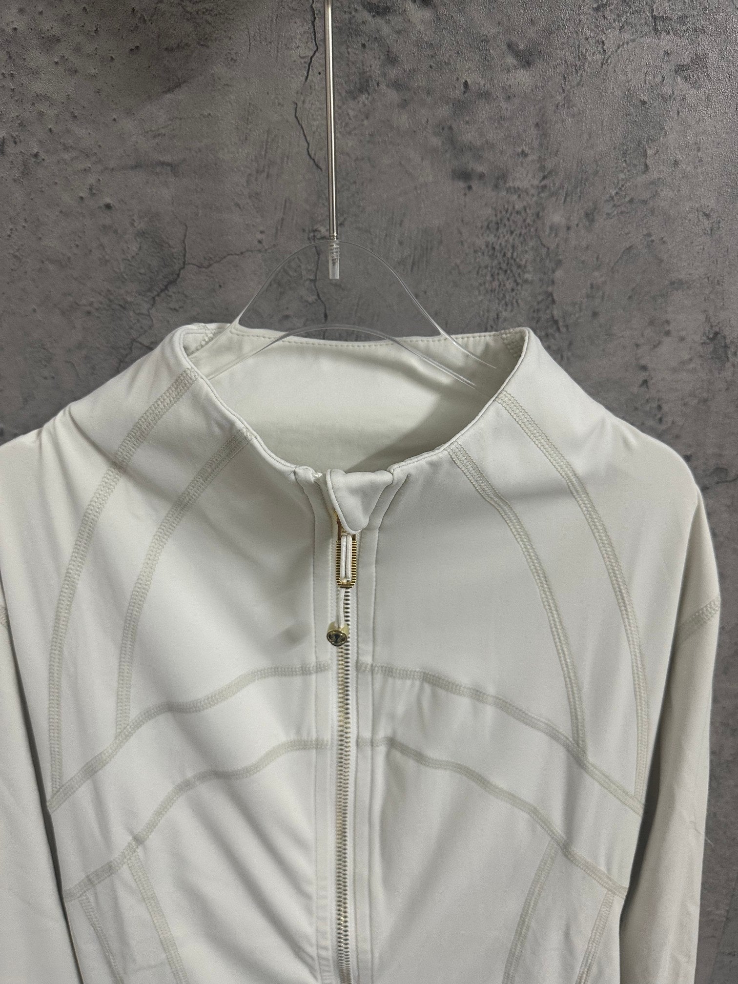 White zip-up jacket front close-up with stand collar and gold zipper hardware