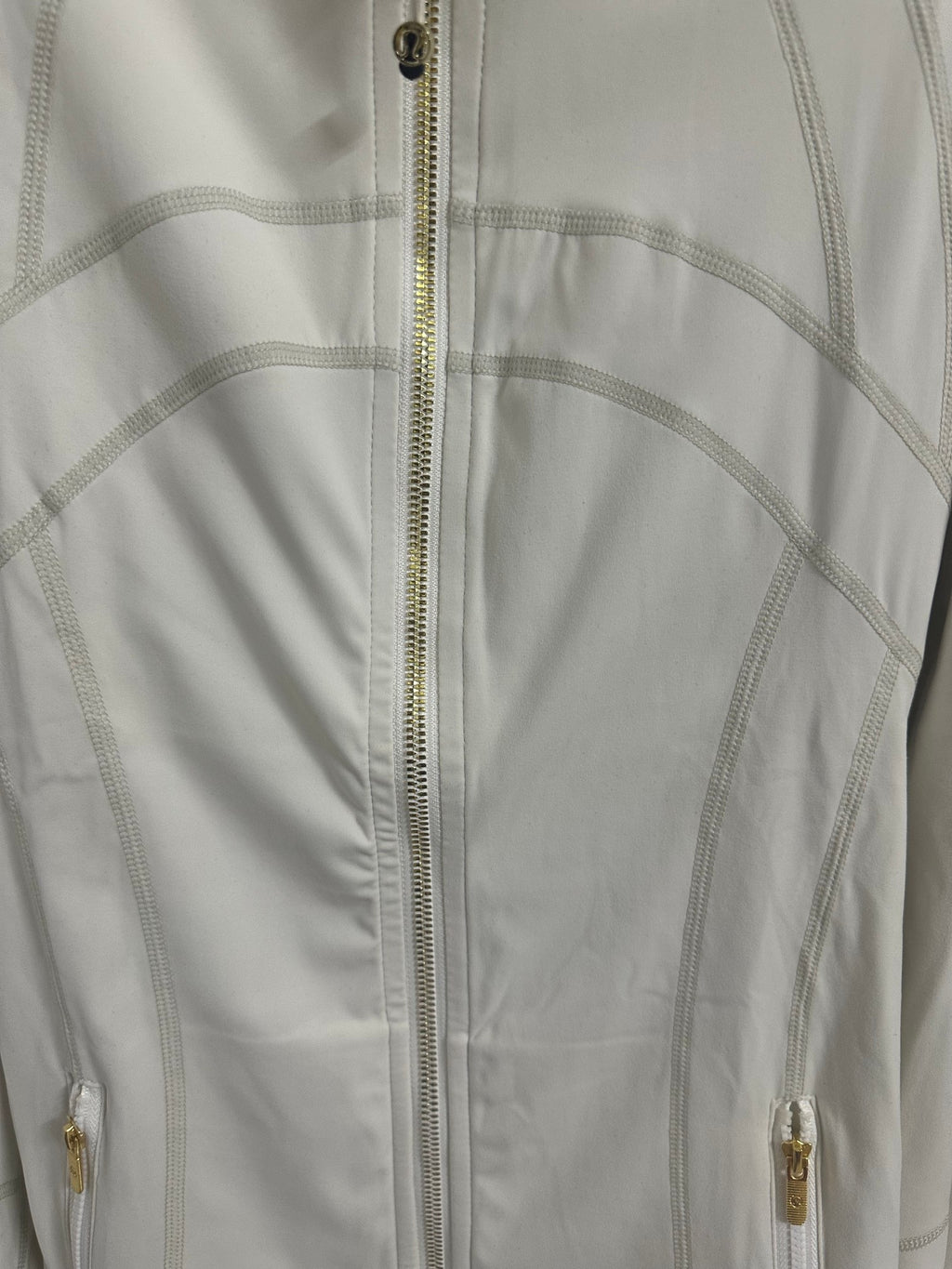 White zip-up jacket close-up, center zipper with gold-tone hardware details
