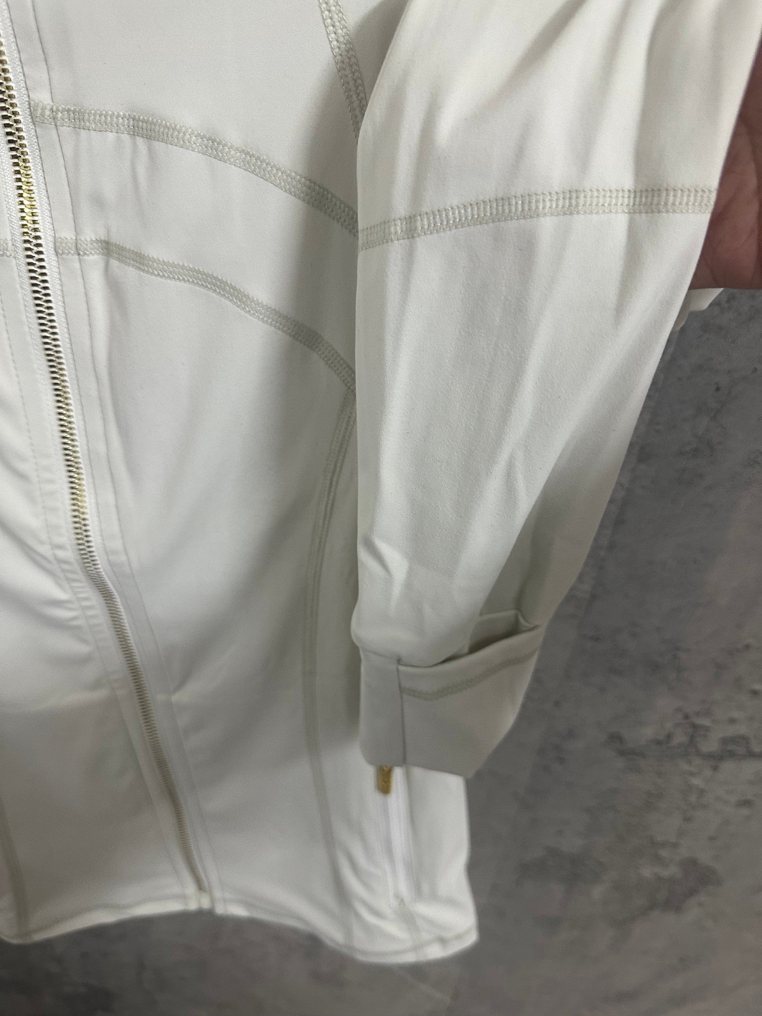 White zip-up jacket sleeve and cuff with gold-tone zipper pull detail