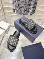 Dior slide sandals on blue box; black base with gray Dior-oblique patterned upper