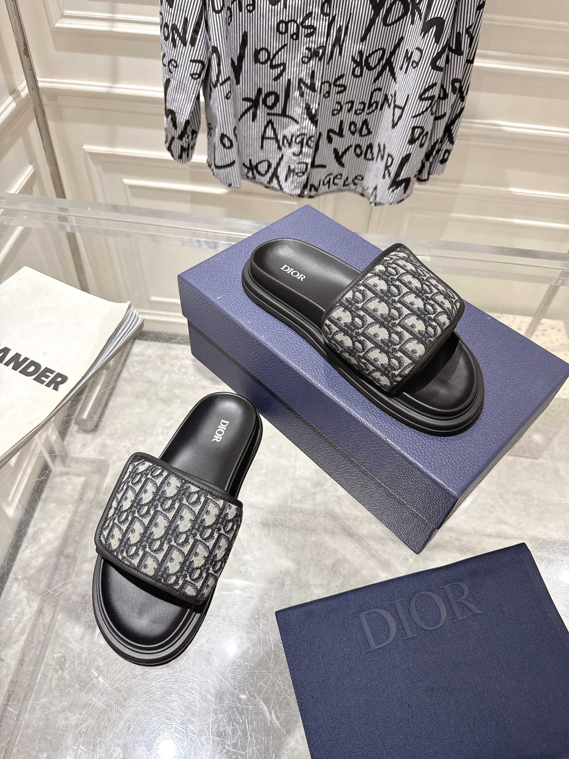 Dior slide sandals on blue box; black base with gray Dior-oblique patterned upper