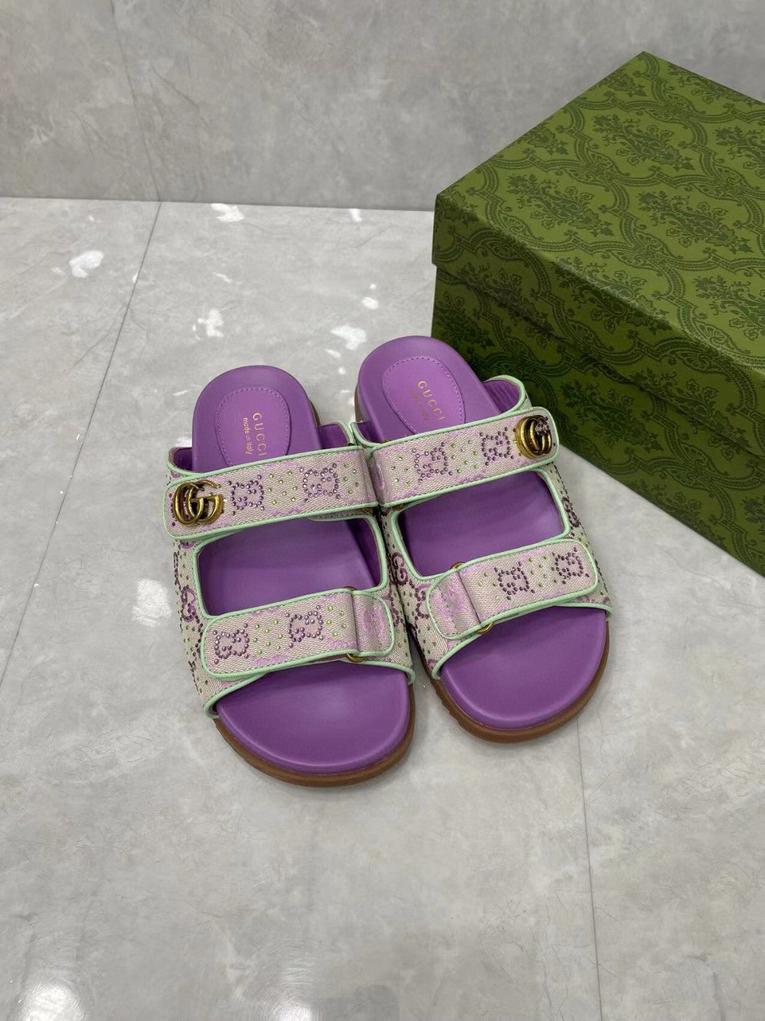 Gucci lilac slide sandals with GG-style print straps and gold-tone buckle, open toe.