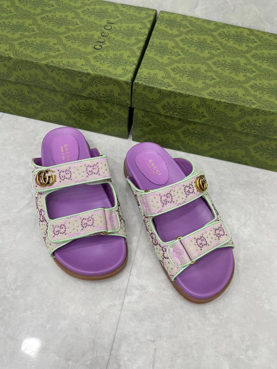 Gucci lilac slide sandals with light pink patterned straps and gold-tone buckle detail.