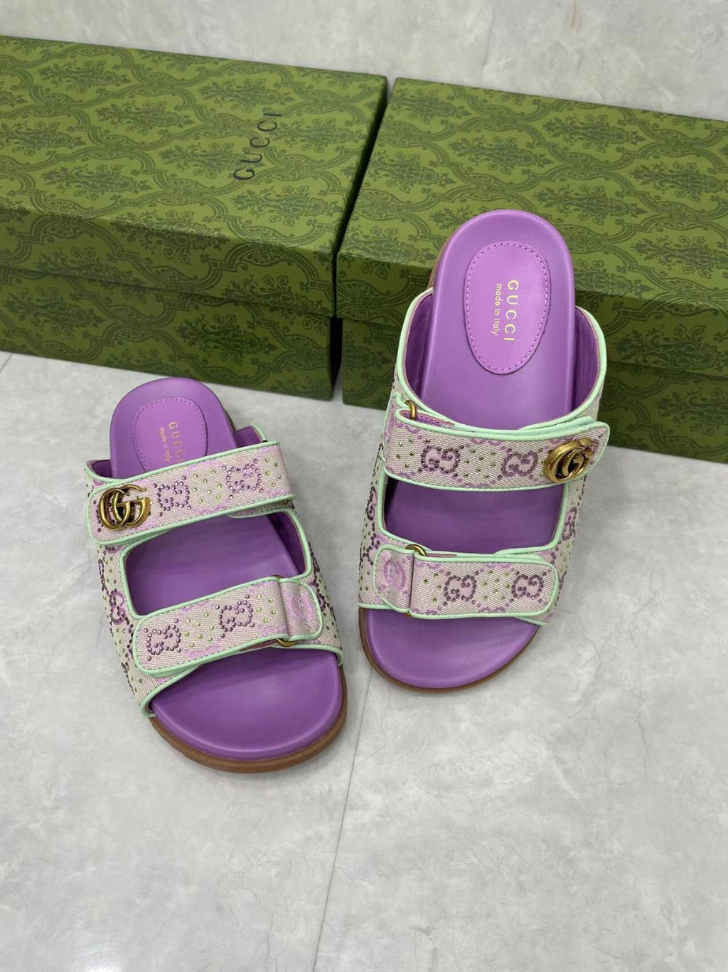 Gucci lilac slide sandals with two cross straps and purple footbeds, gold buckle.