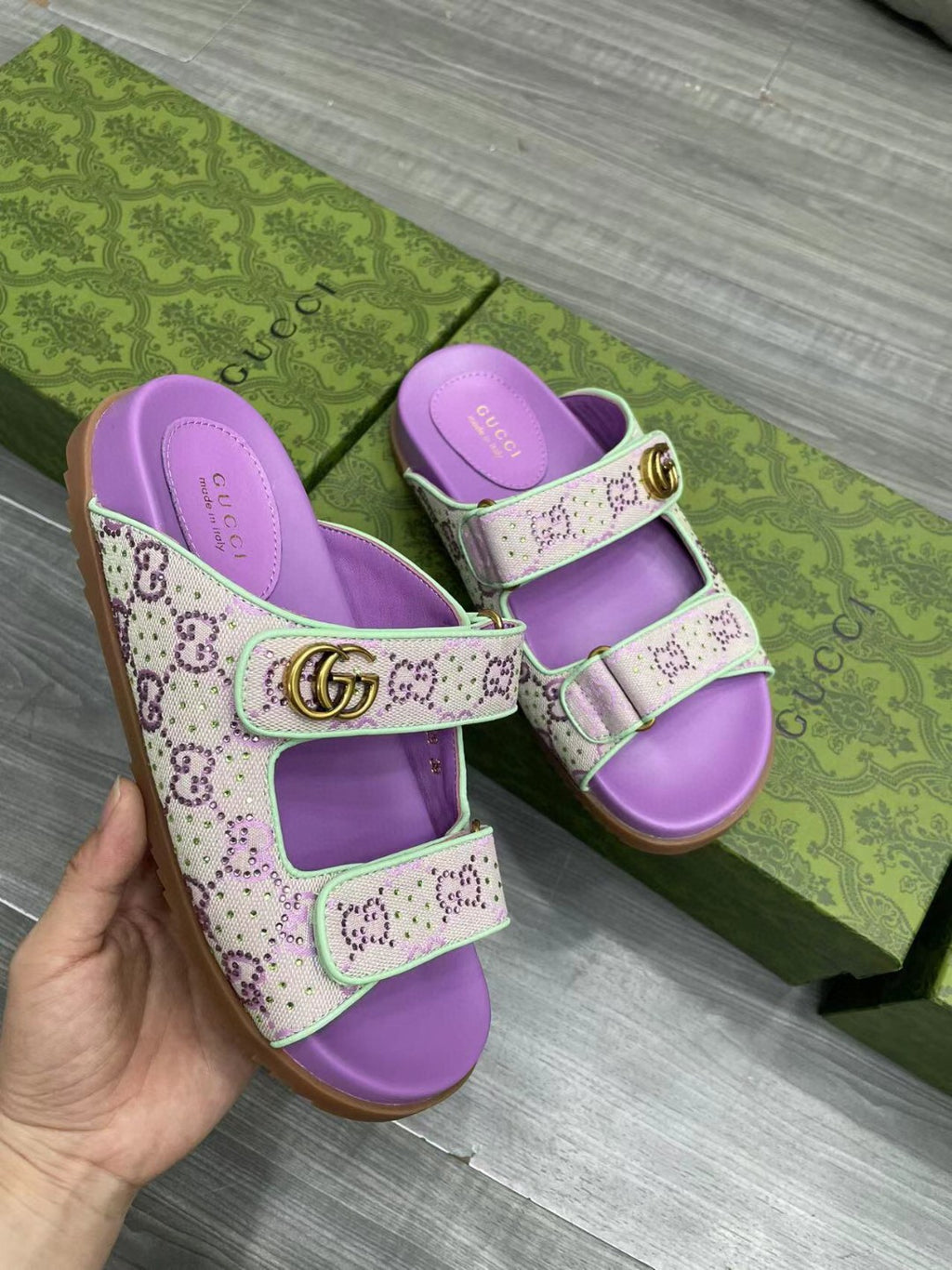 Gucci lilac slide sandals with light pink GG-print straps and gold-tone buckle.