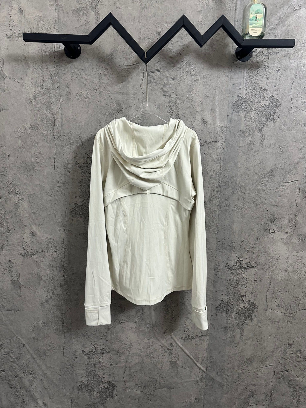 White hooded jacket with draped cowl hood, shown from the back while hanging.