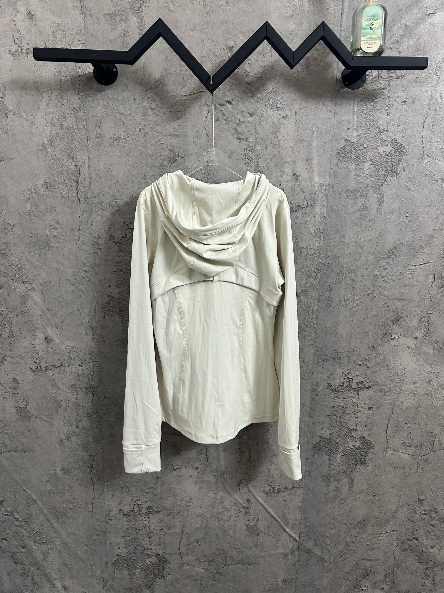 White hooded jacket with draped cowl hood, shown from the back while hanging.