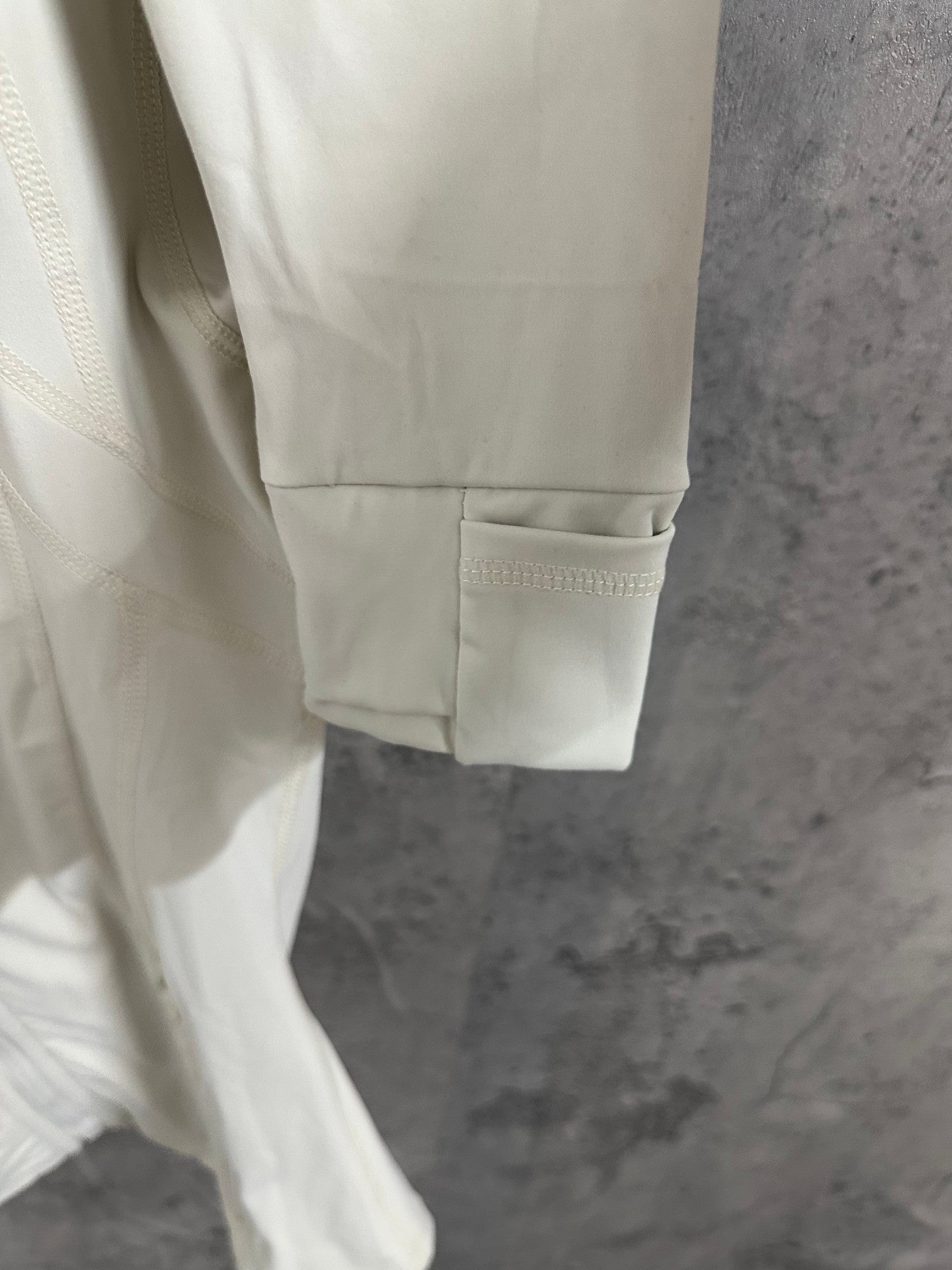 White hooded jacket hem detail with kangaroo-style pocket and long sleeve cuff.