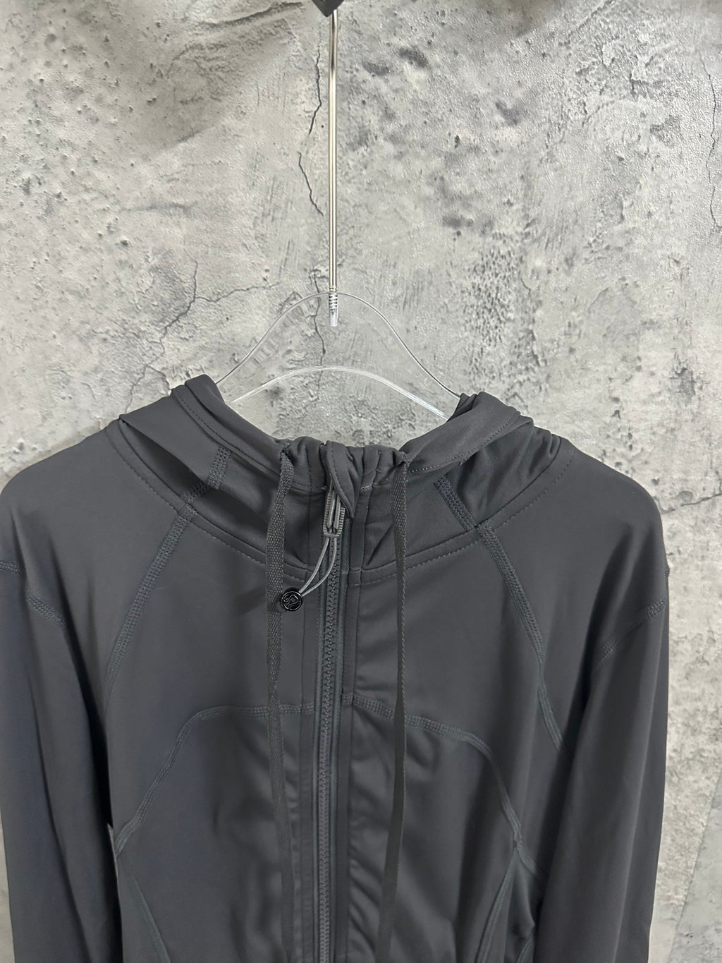 Dark hooded jacket close-up with center zipper and drawcord hood