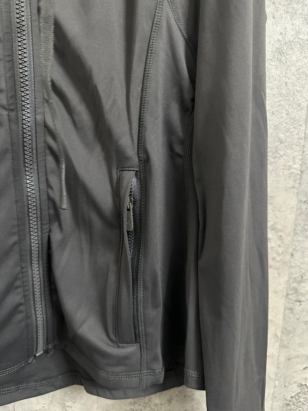 Dark jacket detail with side zipper pocket and smooth outer fabric