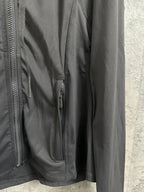 Dark jacket detail with side zipper pocket and smooth outer fabric