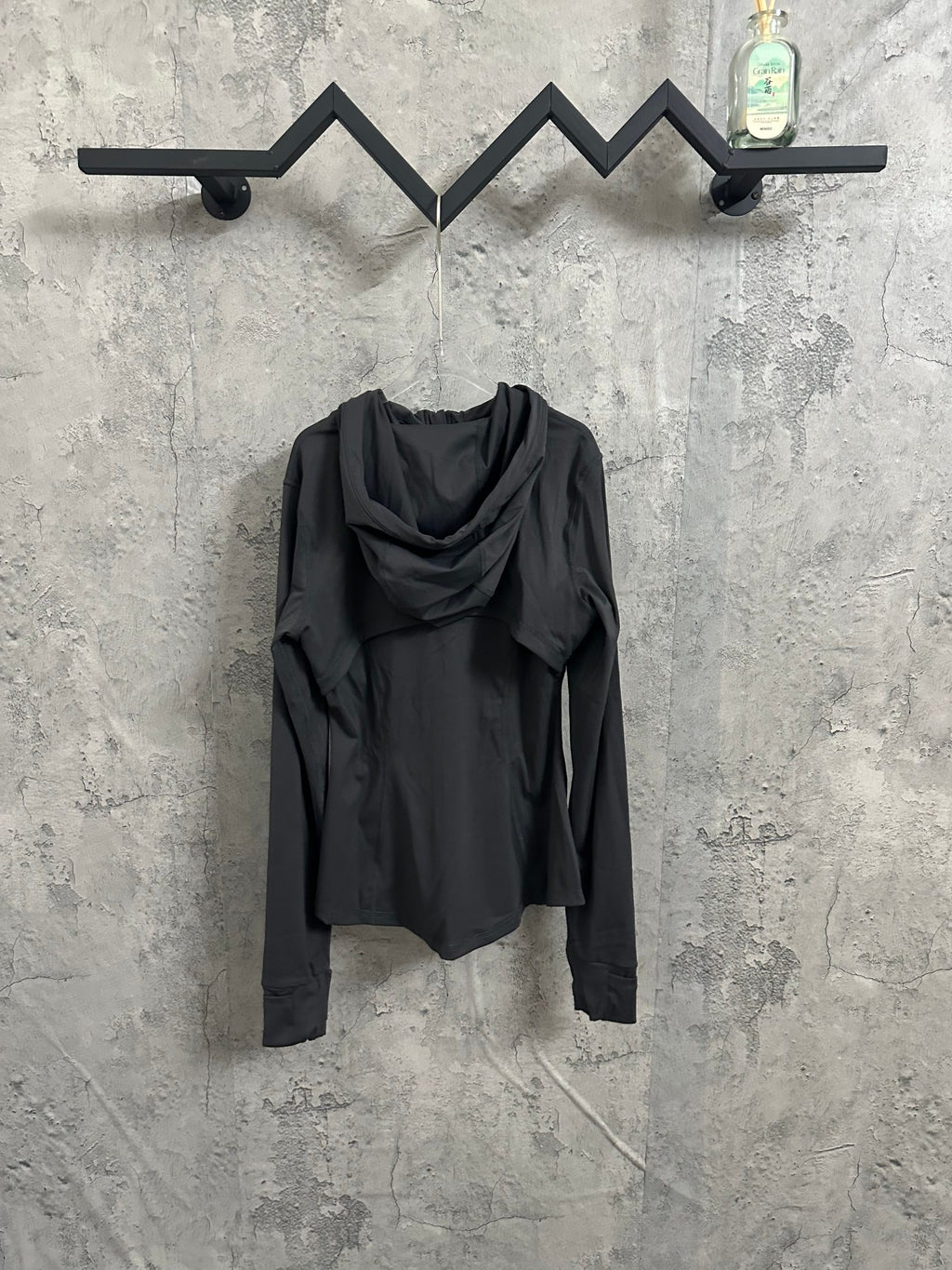 Dark hooded zip-up jacket shown from the back, with drawstring hood