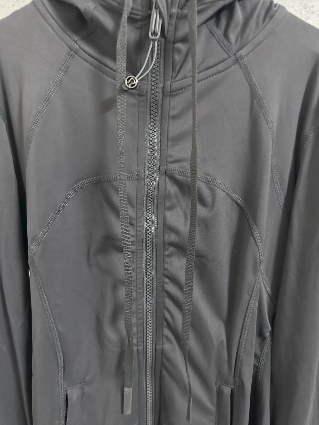 Dark hooded jacket detail with center zipper, drawstrings, and paneled stitching