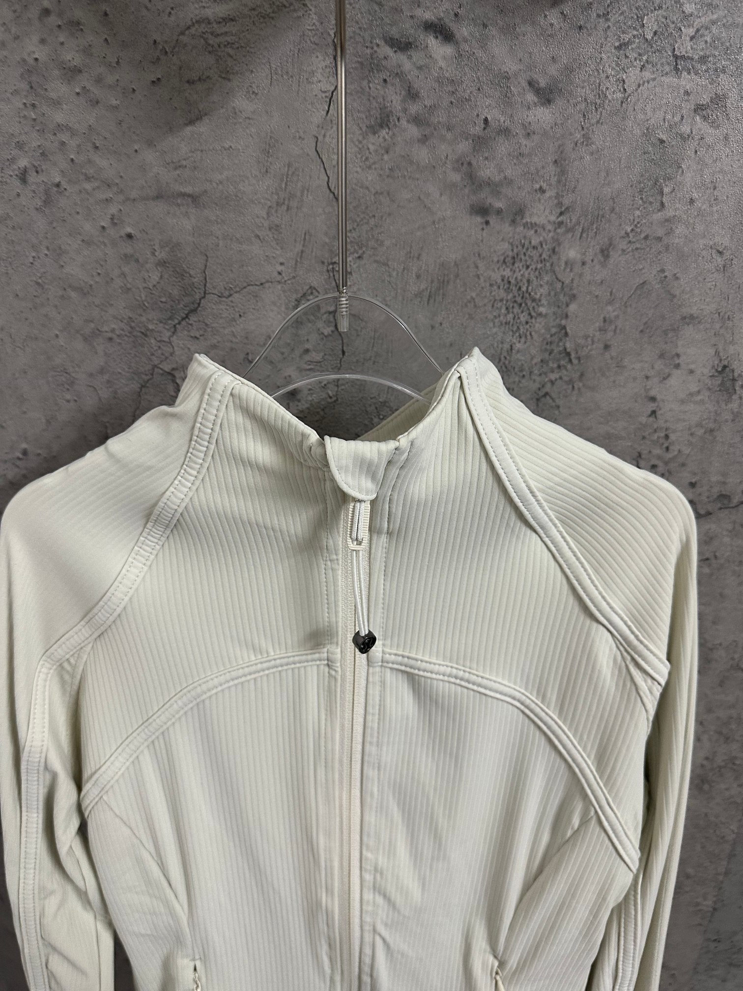 Light cream ribbed jacket showing front zipper, stand collar, and curved chest panels