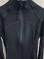 Dark jacket close-up with center zipper, curved yoke seams, and small chest logo