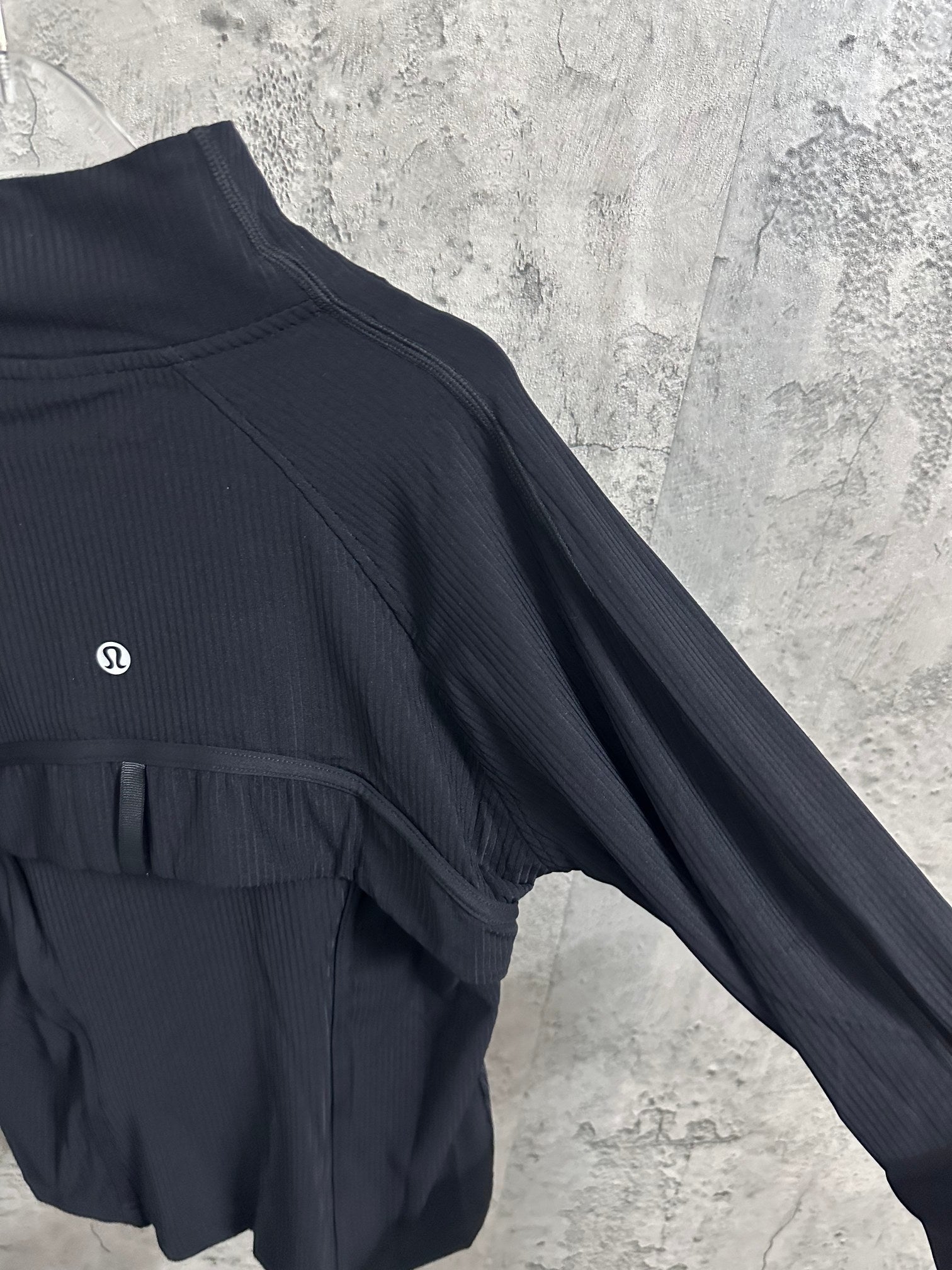 Dark zip jacket with high collar, curved shoulder seams, and chest emblem