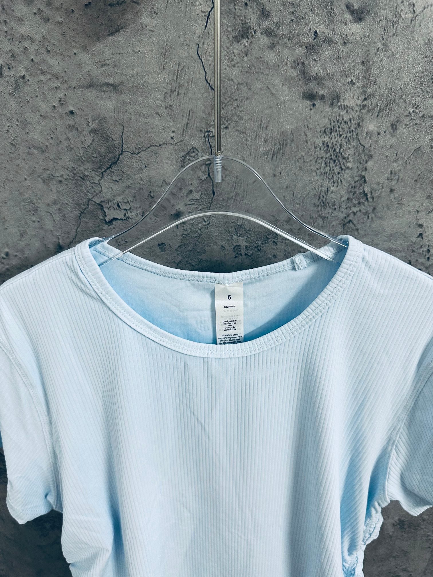 Light blue ribbed crew-neck T-shirt detail with neck seam and small tag on hanger