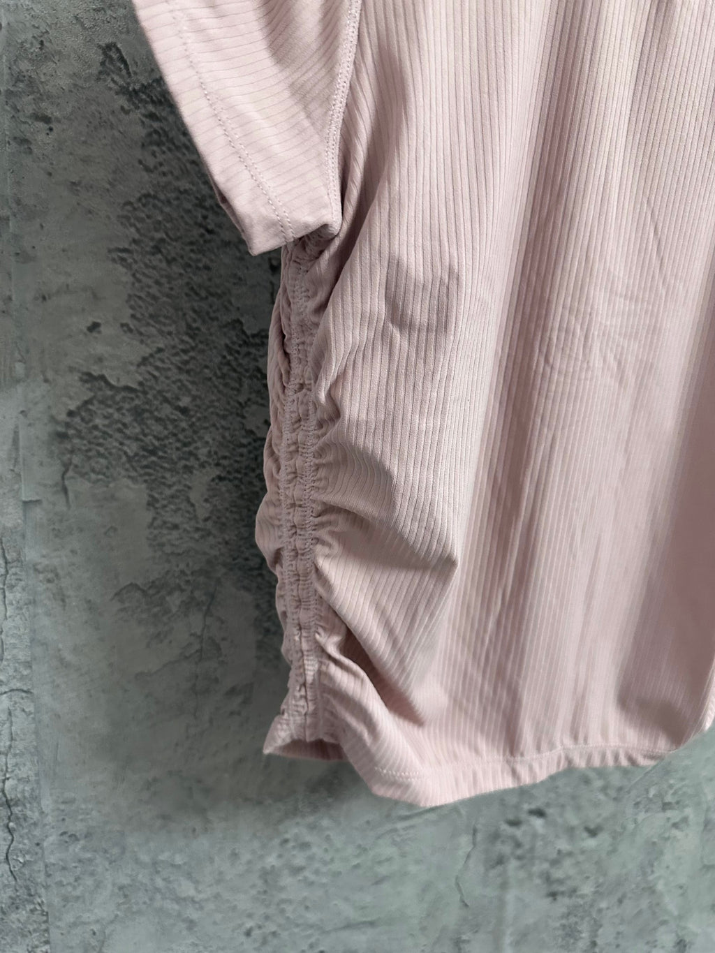 Light pink short-sleeve T-shirt fabric detail with gathered seam at lower side.
