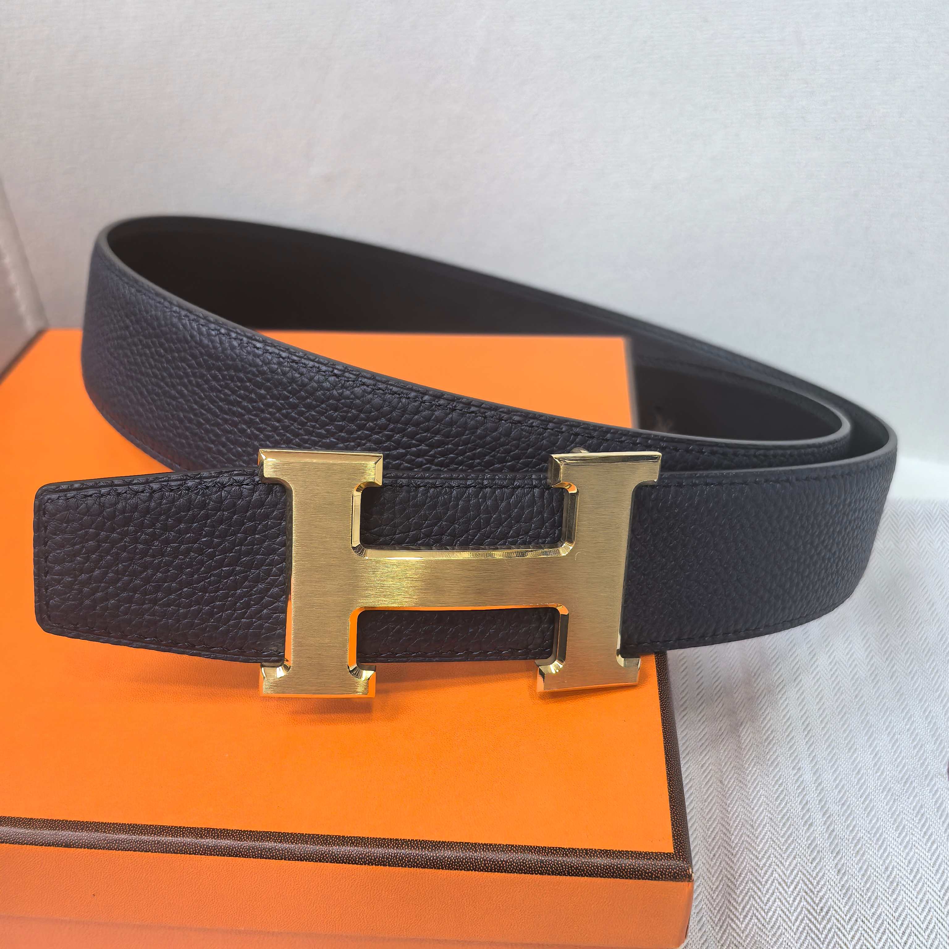 Hermes belt front view: dark leather strap with large gold-tone H buckle