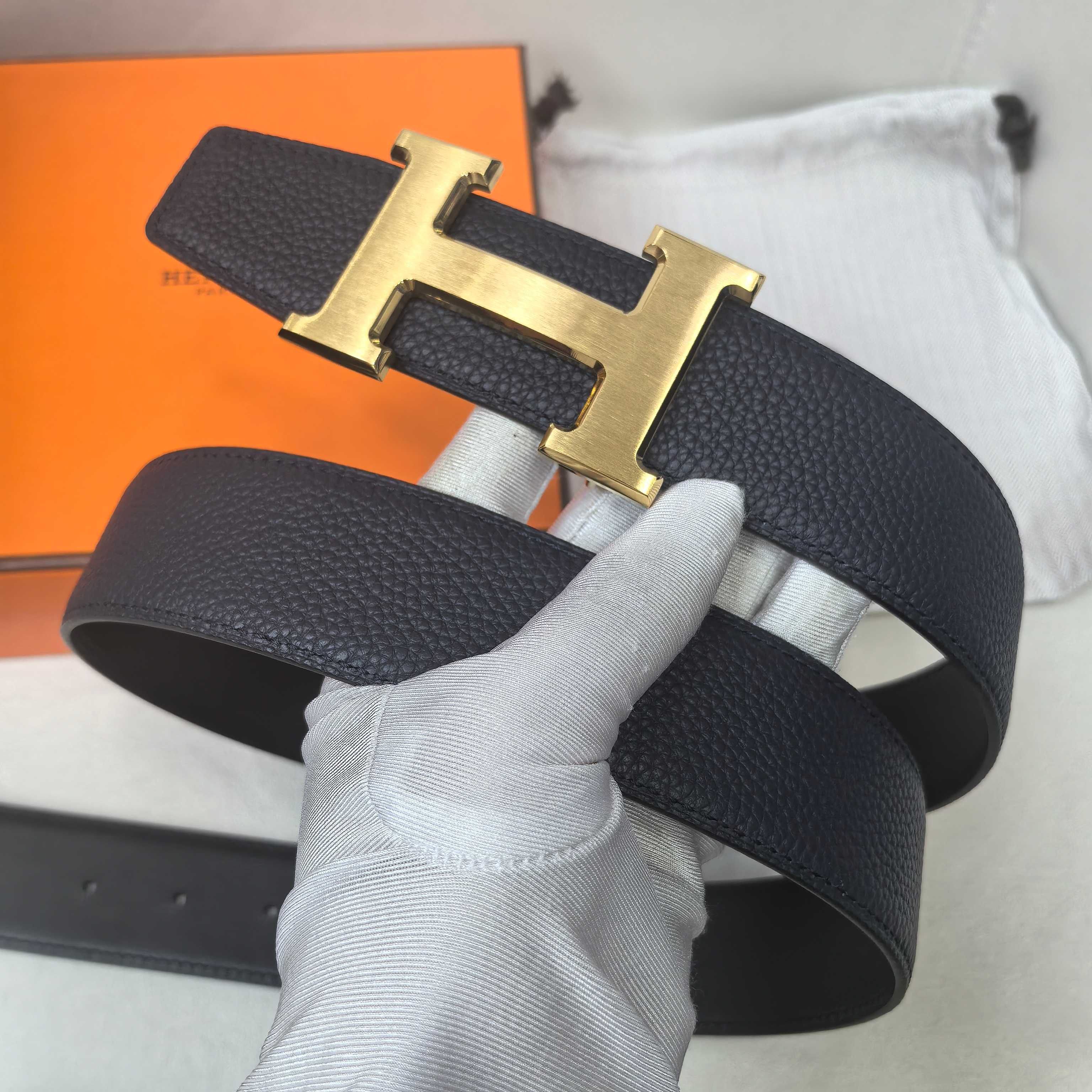 Hermes belt close-up: dark leather strap with gold-tone H buckle centered