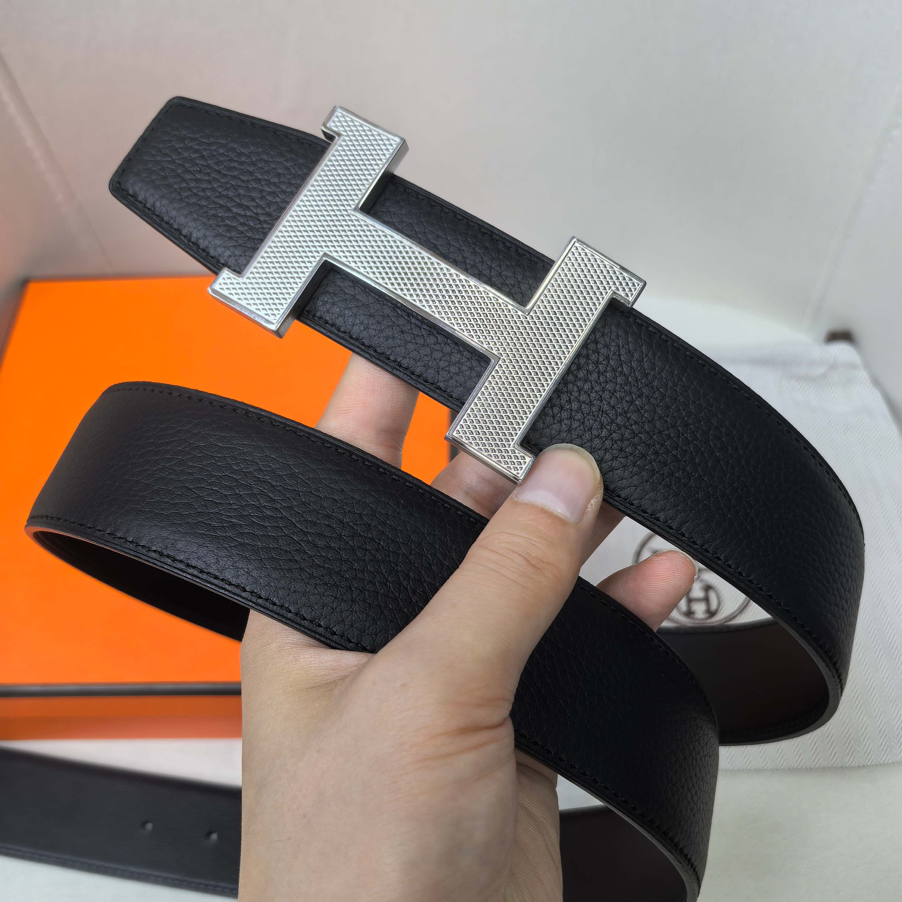 Leather belt with large silver H buckle and dark textured strap, close-up