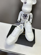 White leather Prada sneakers set on a black shoebox, side and heel visible.