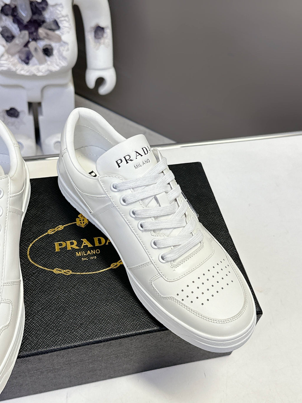 White Prada leather low-top sneaker with perforated toe and lace-up front.