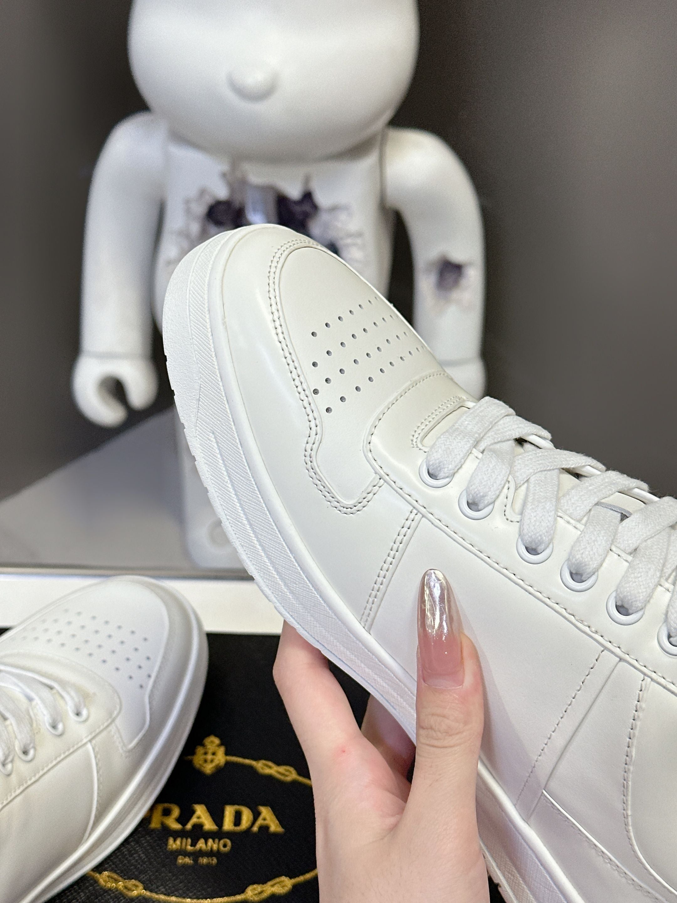 White Prada leather sneaker with perforated side panel and lace-up closure.